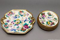 Photo of 10.75 inch octagonal cake plate with gold gilded handles next to six round dessert plates