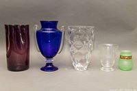 Full set of five vases from left to right: amethyst purple vase, cobalt blue urn, clear etched crystal vase, small clear frosted vase, small green frosted vase with gold band.
