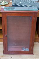 Front view of vintage wooden wall display case with glass door showing wooden frame and metal locking key.