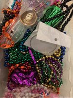 Photo of colorful metallic Mardi Gras bead necklaces in green, purple, and gold, along with a silver circular item and other costume jewelry