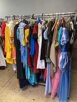 Wide view of multiple colorful Disney-themed costumes hanging on a clothing rack, including dresses with puff sleeves in blue and pink shades and other characters.