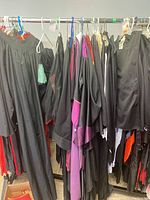 View of multiple Harry Potter themed cloaks and costumes hanging on a clothing rack showing a variety of black robes with different sleeve types and details
