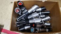 Box full of black and silver light sabers replicas stacked together showing various handle details.