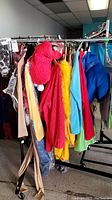 Photo of mascot costumes rack showing red Elmo costume, yellow and blue garments, and other colorful costumes hung on metal rack.