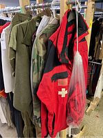 Green and camouflage military-style clothing hanging on a rack with red and black medical jackets bearing white crosses