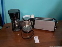 Photo showing the lot contents including the Closer 4-slice toaster, Salton glass kettle, Sunbeam coffee maker, and plates and cups in the background.