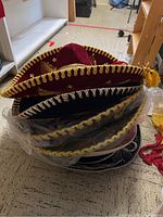 Stack of sombrero hats showing burgundy and black hats with gold embroidery and tassels.