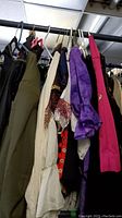 Multiple traditional-style costume clothing pieces hanging on a rod, including items in black, purple, cream, and pink.