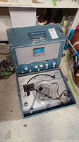 Blue vintage phonograph record player with speaker and control panel in portable case open, showing turntable and tonearm.