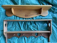 Top-down view of two wooden shelves on blue fabric, showing solid back shelf and open frame shelf with heart cutouts and peg hooks.