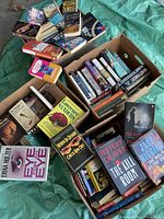 Photo shows four boxes filled with used books, various titles and authors visible including Jeffery Deaver and Martha Grimes.