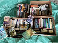 Four boxes filled with used fiction books by various authors including Maeve Binchy as visible on covers and spines.