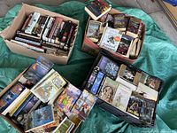Four boxes full of used paperback books with visible covers and spines showing science fiction and fantasy titles and authors.