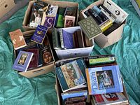 Five cardboard boxes full of assorted used books including literature, stress relief, history, and guides.