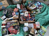 Photo showing multiple boxes filled with books by various authors placed on a green cloth.