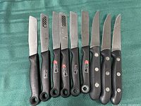 Photo of nine Henckel branded knives on green fabric background, showing blade edges with signs of wear and different handle styles.