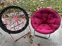 Photo showing both chairs side by side, one bungee cord dish chair and one red cushioned saucer chair on concrete outdoors with leaves scattered around.