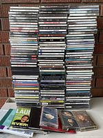 Large stacks of used audio CDs showing spines with various music titles in multiple genres.