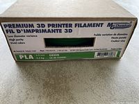 Closed cardboard box labeled with 'Premium 3D Printer Filament' by MG Chemicals, showing key product details like 3.0 mm diameter, 0.5 kg weight, green color, low diameter variance, and high purity.