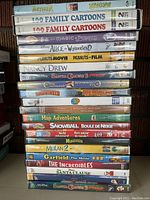 Stack of kids DVD cases showing colorful spines and some titles readable such as Arthur, Barbie Magic of Pegasus, Disney Alice in Wonderland, Peanuts Movie, Nancy Drew, Mulan 2, Garfield The Movie, The Incredibles, The Santa Clause, Madagascar, Snowball, Nick Jr. World Animal, and triplets of family cartoons DVDs.