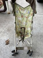 Front view of the stroller showing green fabric seat and canopy with Winnie the Pooh characters, safety harness straps attached.