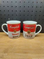 Two ceramic coffee mugs side by side featuring the Campbell's Condensed Tomato Soup design, showing front views of both.