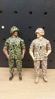 Two Canadian Forces military figures standing on a wooden surface against a black pegboard background, showing full body view and details of uniforms and helmets.