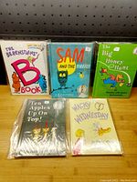Five children's books displayed on wooden surface with visible titles and colorful covers in plastic sleeves