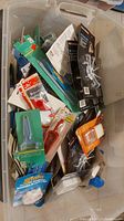 Various small household and hardware items in original packaging inside a clear plastic storage bin