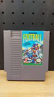 Front view of the gray Nintendo NES game cartridge with Play Action Football label showing a colorful cartoon football scene.