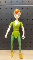 Front view of the Disney Peter Pan figure toy showing detailed facial features, green clothing, and yellow shoes against a black pegboard background.
