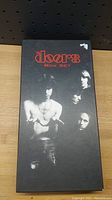 Black box set cover for The Doors featuring a photo of the band and red lettering on a black background.