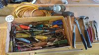 Box filled with various screwdrivers, hammers, and pliers spread around with a visible yellow rope above