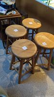 Four solid wood stools arranged together showing round seats and wood grain, placed on carpet.