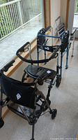 Four collapsible walkers including two with seats and brakes and two without, arranged indoors near a window.