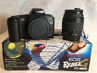 Canon EOS Rebel G camera body with attached lens caps placed on original Canon EOS Rebel G kit box.