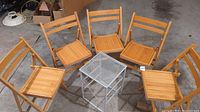 Five folding wood chairs arranged in a circle around a metal side table