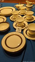 Overview of plates, teacups, saucers, creamer and sugar bowl with intricate gold and black patterns on white china.