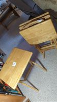 Two of four folding TV tables shown; one table folded and stacked against the couch and the other set up on the floor.