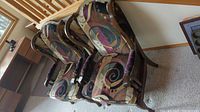 Two solid wood wingback chairs with reupholstered multicolor abstract swirl pattern fabric and wood cane inset sides, shown together from front angle.