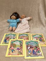 Two original 1982 Cabbage Patch Kids dolls and seven illustrated story books with colorful covers.