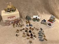 Full lot showing various miniature cottages, music box, and numerous Wade figurines arranged on a neutral cloth background.