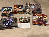 Photo showing entire lot including D&D Forgotten Realms Drizzt & Guenhwyvar box, Pathfinder Adventure Card Game, Keyforge deck, Pandemic core game and expansion, and the Lost Mine of Phandelver manual spread out on carpet.