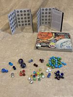 Overview photo showing two open state quarter collecting cases, various marbles laid out, and a coin collecting book.