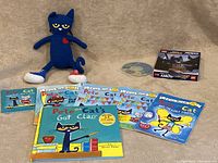 Plush blue Pete the Cat with yellow eyes and red patch on chest, displayed with 7 Pete the Cat themed children's books.