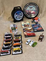 Full view of the lot including Pixar Cars neon clock with red light effect, Hot Wheels storage box, multiple Maisto and Matchbox diecast cars in unopened packages, Dusty Crophopper toy, Mater book, and two Cars DVDs.