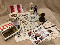 Photo shows entire lot with all items arranged on beige fabric including books, magazines, figurines, plates, fabric with presidential portraits, US flag