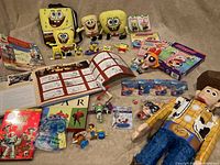 Overview of SpongeBob plushes, assorted toys from Pixar including Toy Story characters, Powerpuff Girls puzzle and plush, and a Pixar history album in French.