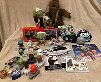 Wide view of Star Wars collectible items including plush, lunch box, toys, action figures, vehicle models, and booklets.