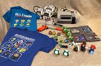 Full lot overview showing NES console, controllers, 5 game cartridges, numerous Mario-themed character figures, and two T-shirts